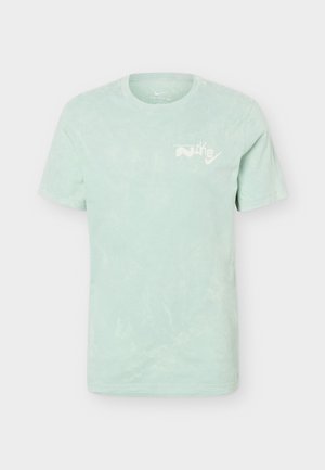 T-shirt vert clair à manches courtes et col rond avec logo et texte Nike blancs sur le côté gauche de la poitrine, présenté sur un fond uni.