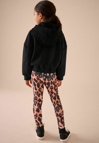 Sweatshirt noir à capuche avec taille élastique, associé à des leggings légers à imprimé léopard rose et des baskets montantes noires.