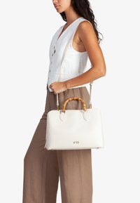 Borsa a mano bianca in pelle con manico in bambù, dettagli dorati e due tracolle removibili. Texture liscia, forma rettangolare, logo del marchio visibile in modo discreto.