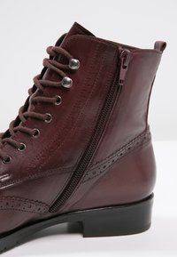 Botín de cuero burdeos hasta el tobillo con cremallera lateral, puntera redonda, cordones en la parte delantera, detalles de brogue y un tacón bajo negro.
