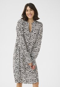Schwarz-weiß gemustertes Kleid mit V-Ausschnitt, langen Ärmeln und gerafften Bündchen. Leichtes Material mit einem abstrakten, wellenförmigen Design.