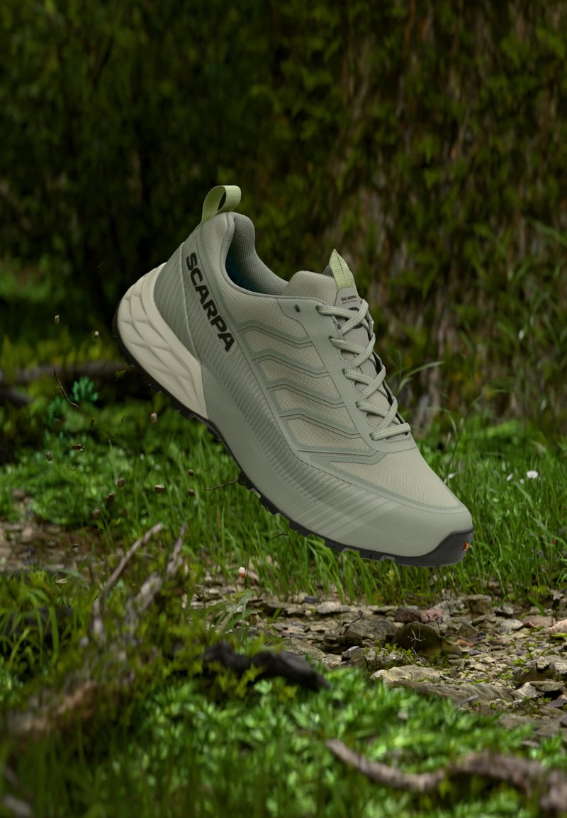 Ελαφρύ πράσινο πεζοπορικό παπούτσι Scarpa στον αέρα πάνω από ένα δασικό μονοπάτι με γρασίδι, πέτρες και σκορπισμένα φύλλα.