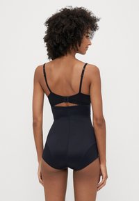 Bodysuit preto com alças ajustáveis, decote em forma de onda e um design sem costuras. Textura suave com costura mínima e uma silhueta ajustada.