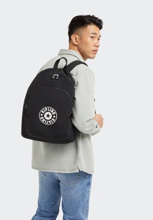 Black backpack with a rounded shape, featuring a circular white logo, zippered compartments, and padded shoulder straps. Textured fabric.