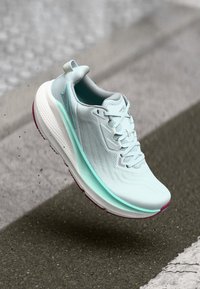 Basket de course bleu clair avec des accents turquoise en l'air au-dessus d'une route en asphalte avec des lignes blanches, soulevant de petites particules de poussière.