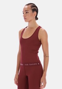 Bordó sportosan szabott trikó mély kivágással és széles pántokkal. Anyaga rugalmas és testhez simuló, márkázott derékpánttal.