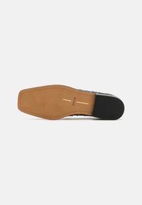 Black shoe flat sole with a smooth, tan upper section and subtle markings. Features a rounded shape and textured grip on the heel.