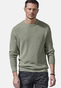 Strickpullover mit Rundhalsausschnitt in Hellgrün, mit gerippter Textur, langen Ärmeln und lockerer Passform, kombiniert mit dunklen Jeans.