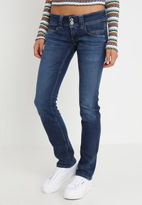 Smala blå denimjeans med två framfickor, knäppning med knapp och kontrasterande sömmar. Bärs med vita sneakers.