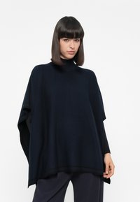Poncho blu scuro con colletto alto, realizzato in materiale morbido. Presenta una silhouette ampia e una texture sottile, adatto per essere indossato a strati.