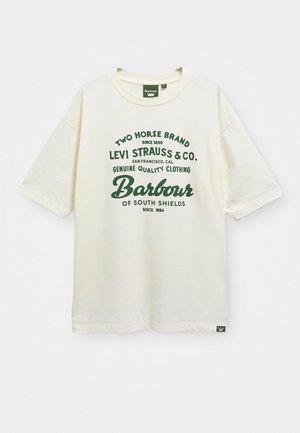 T-shirt en coton crème à manches courtes, avec texte et logo verts, décolleté rond et une étiquette en bas à gauche.