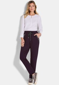 Witte lange mouw top met een keyhole halslijn, gecombineerd met donkerpaarse joggingsbroeken met zijzakken en een trekkoord.