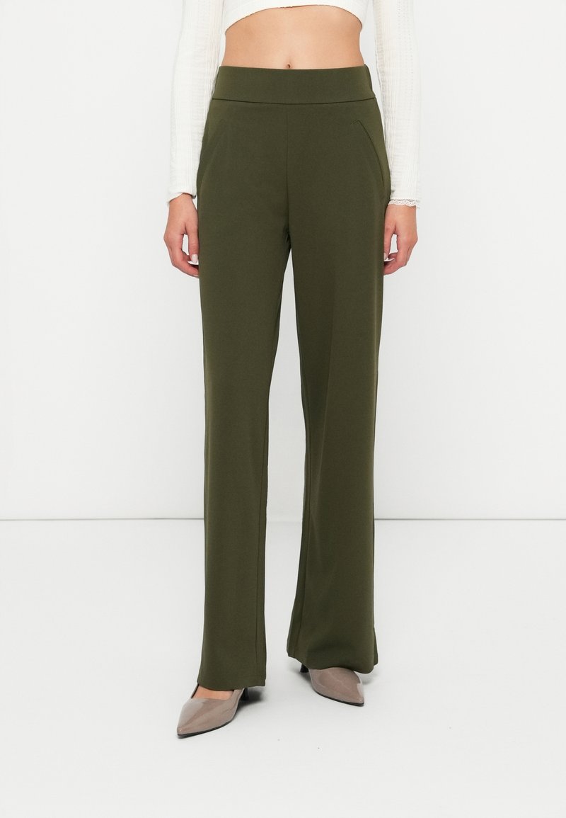 Pantalon à jambes larges vert olive en tissu lisse, avec une taille haute élastique et des poches latérales, accompagné de talons beiges.