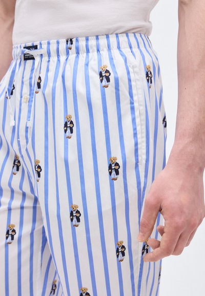 Άνδρας που φοράει λευκό και μπλε παντελόνι με ρίγες, με σχέδιο από μικρά αρκουδάκια ντυμένα με ναυτικά σακάκια και λευκό παντελόνι.