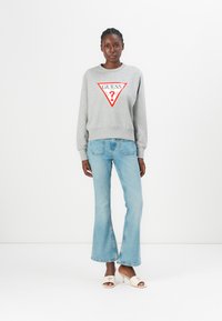 Grijze sweatshirt met rood driehoeklogo, gecombineerd met lichtblauwe flared jeans en crèmekleurige open teen hakken. Eenvoudig ontwerp, casual stijl.