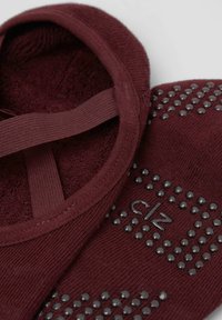 Burgundy slip-on socks with textured grip dots and a soft, plush interior. Features elastic strap and subtle logo detail.