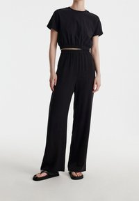 Černý dvoudílný outfit s krátkým tričkem a volnými kalhotami. Obsahuje nařasený pás, hladkou látku a jednoduchý design.