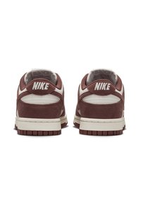 Scarpe da ginnastica Nike con tomaia in pelle scamosciata marrone, dettagli in pelle bianca e una suola intermedia color crema. Presentano una suola esterna in gomma testurizzata e un marchio ben visibile.