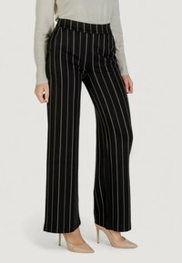 Černé pruhované širší kalhoty s vysokým pasem, se svislými zelenými pruhy a hladkou texturou látky. V kombinaci se světle zbarvenými podpatky.