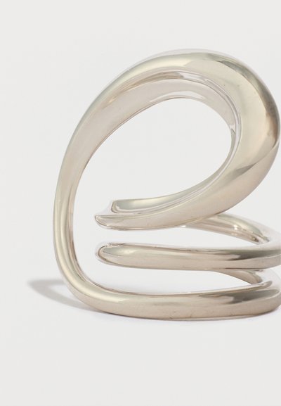 Ασημί δαχτυλίδι από μέταλλο με λείο, κυρτό σχέδιο που διαθέτει τρεις εμπλεκόμενους βρόχους. Η αντανακλαστική, γυαλισμένη επιφάνεια ενισχύει την κομψή του εμφάνιση.
