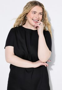 Schwarzes kurzes Kurzarmkleid aus weichem Material, mit rundem Ausschnitt und lässiger Passform. Es hat einen dezenten Fall und ein schlichtes Design ohne Muster.