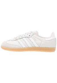 Zapatilla blanca de cuero con puntera de ante, tres franjas blancas, suela de goma y costuras tonal. Presenta elementos de diseño clásicos.