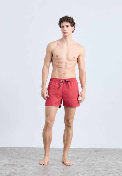 Röda badshorts i lätt tyg med elastisk midja och dragsko. Mjuk textur, kort längd och enkel design.