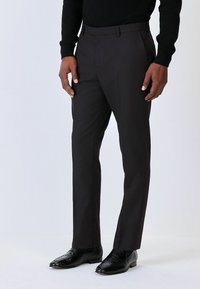 Dopasowane czarne spodnie wizytowe o gładkiej teksturze, slim fit i prostym przodzie, w połączeniu z czarnymi butami o teksturze krokodyla.