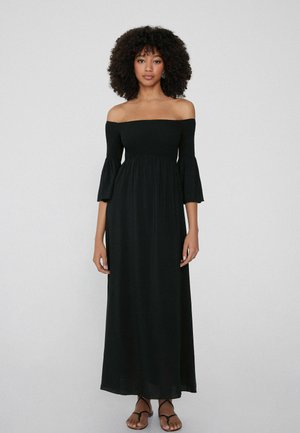 Schwarzes Maxikleid mit schulterfreiem Design, ausgestelltärmeligen, gerafftem Oberteil, fließendem Rock und leichtem Stoff, kombiniert mit schwarzen Sandalen.