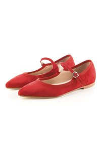 Zapatos planos de ante rojo con puntera afilada, una correa delgada en el tobillo y suela plana. El interior es de un suave color beige.