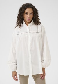 White blouse with a high collar, button-down front, and puffed sleeves. Lace detailing near the chest and elastic at sleeve cuffs.