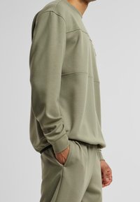 Sweat-shirt vert olive avec col rond et manches longues. Caractéristiques : coupe décontractée, tissu texturé, poches latérales dans les coutures.