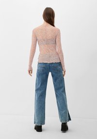 Langärmliges, transparentes Oberteil mit einem wirbelnden Muster in Pfirsich und Beige, kombiniert mit hochgeschnittenen, hellblauen Jeans und schwarzen Plateaustiefeln.