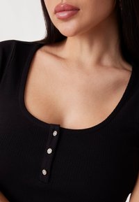 Svart ribbet skjorte med scoop-hals, som har tre dekorative knappelukkinger pyntet med rhinestones.