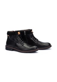 Botas de tobillo de cuero negro con un acabado suave, que cuentan con un diseño de cordones, cremallera lateral, suela roja en contraste y un detalle de hebilla.