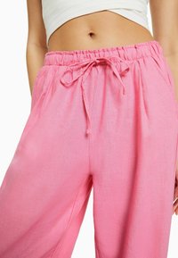 Pantalones ligeros de mezcla de lino en color rosa que cuentan con una cintura con cordón, bolsillos laterales y un corte holgado para mayor comodidad. La textura parece suave y lisa.