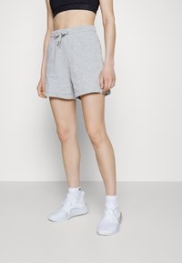 Shorts de sport gris avec une ceinture élastique et un cordon de serrage. Présentent une texture douce et une coupe droite, associés à des baskets blanches.