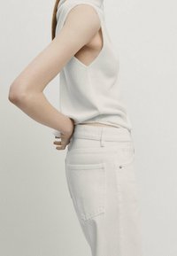 White sleeveless knit top with a v-shaped neckline paired with high-waisted white jeans featuring back pockets and a seamless design.