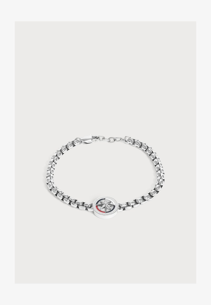 Bracelet chaîne en argent avec un pendentif boussole rond avec un motif étoile et un accent rouge sur fond blanc.