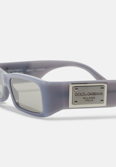 Occhiali da sole con tonalità grigia e montatura morbida in plastica viola. Presentano una piastra del logo metallica sul lato e un design rettangolare elegante.