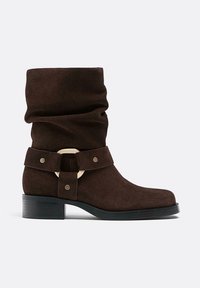 Bottine en suede marron avec un design froncé, dotée d'une sangle décorative avec une boucle circulaire métallique et un petit talon carré.