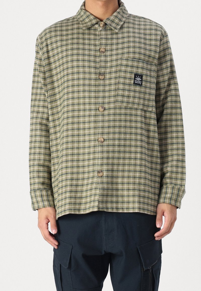 Grön rutigt skjorta med knäppning fram, krage och bröstficka med en logotagg. Tillverkad av textil med synlig sömnad.