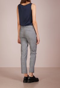 Haut sans manches bleu marine associé à un pantalon gris à carreaux coupe slim et des chaussures noires à lacets, doté d'un tissu lisse et d'une conception structurée.