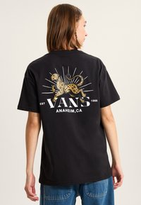 Camiseta de algodón negra con un gráfico de leopardo dorado y acentos de rayos de sol. En el frente lleva la inscripción "VANS" y "ANAHEIM, CA" en letras blancas.