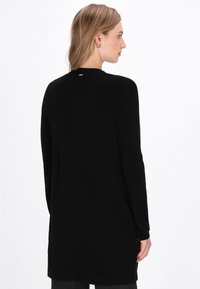 Maglietta nera a maniche lunghe con una vestibilità comoda, scollatura rotonda e tessuto morbido. Presenta un piccolo dettaglio del logo sul retro, senza motivi prominenti.