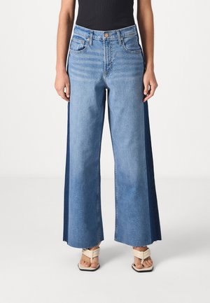 Vaqueros de pierna ancha con una mezcla de denim azul claro y oscuro. Cuenta con bolsillos frontales, cierre de botón y dobladillos deshilachados. Material: algodón.