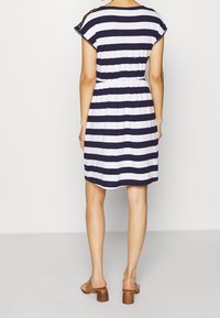 W paski sukienka w granatowo-białym kolorze z bawełny, z krótkimi rękawami, elastyczną talią i długością do kolan. Widoczne brązowe sandały na obcasie.