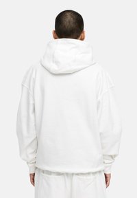 Weißer, übergroßer Hoodie mit großer Kapuze, fallenden Schultern, gerippten Bündchen und glatter Textur. Dazu passend weiße Hosen.