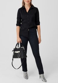 Schwarzes Hemd mit Knöpfen, dunkle Jeans und schwarze Handtasche mit weißen Akzenten. Silbern gefärbte, schlangenlederartige Stiefeletten runden das Outfit ab.