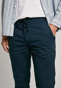 Mornarji modri hlače s stransko vrvico z gladko teksturo, ki imajo stranske žepke in sproščen kroj, v kombinaciji zlahka črtasto srajco.